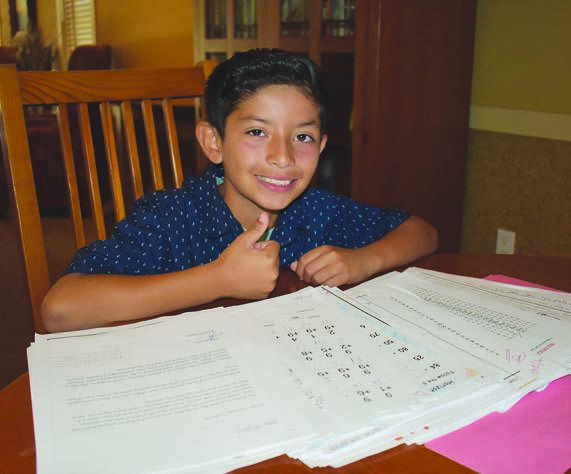 Daniel gives a thumbs-up beside his schoolwork in the 2023 annual report.