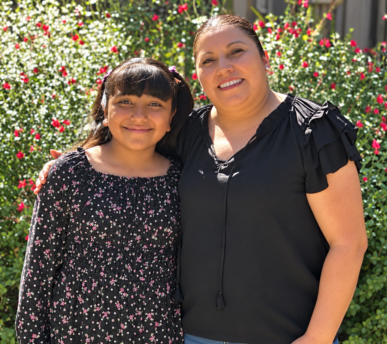 An adult and child smiling together outdoors.