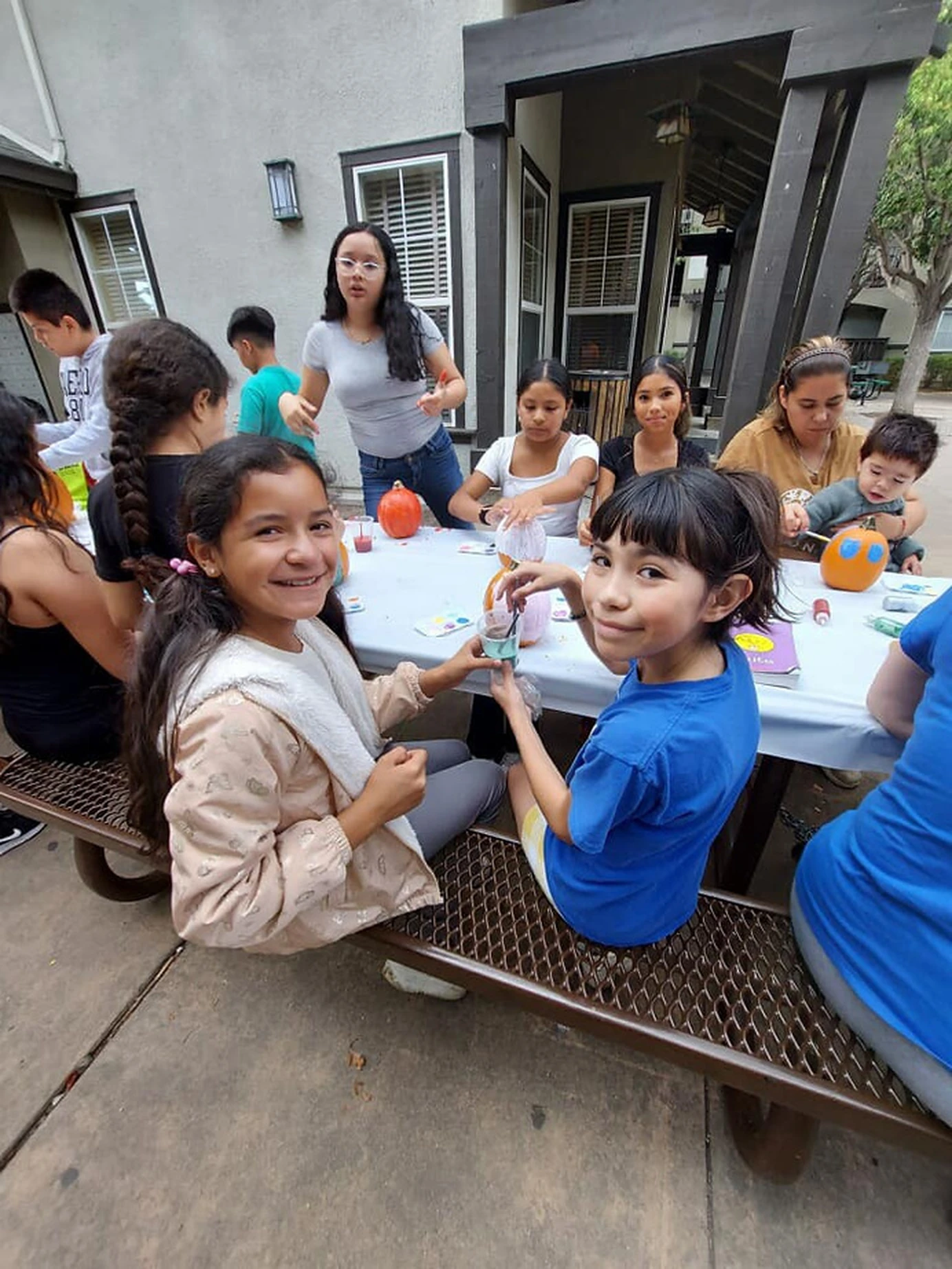 Children and adults decorate pumpkins together around an outdoor table.